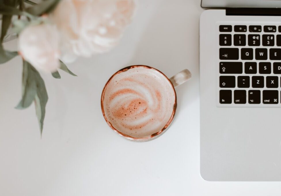 Coffee with swirled milk next to a laptop and white roses on a white desk. Photo by Hayley Kim.
