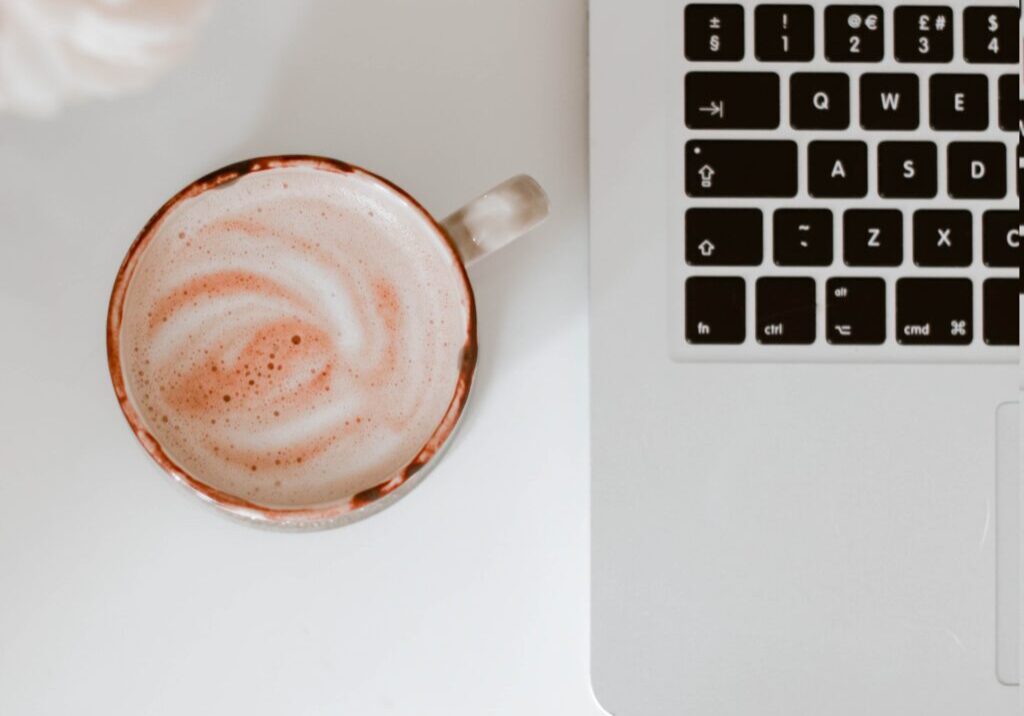 Coffee with swirled milk next to a laptop and white roses on a white desk. Photo by Hayley Kim.
